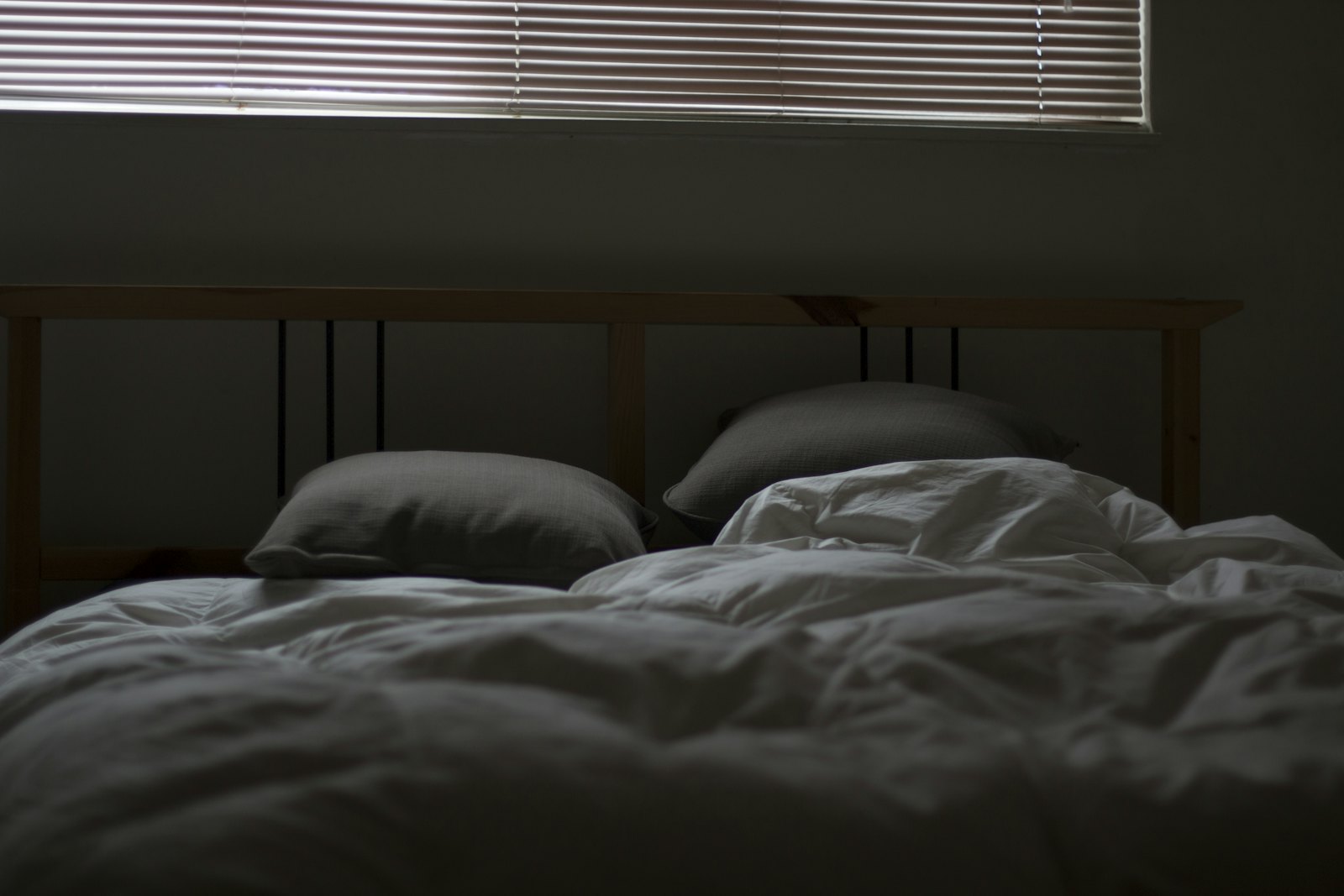 Unmade bed with white and grey bedding beside a window