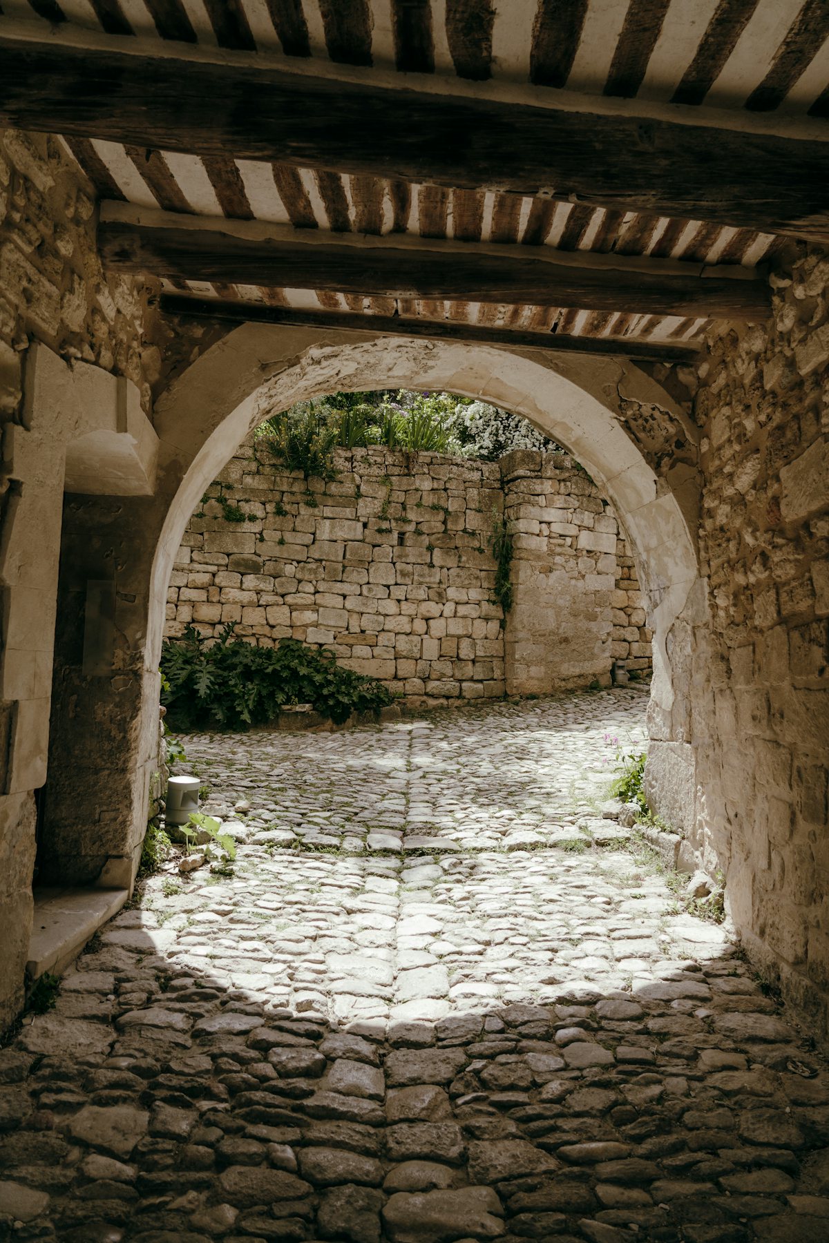 Stone walkway passing under a stone arch into a sunlit courtyard