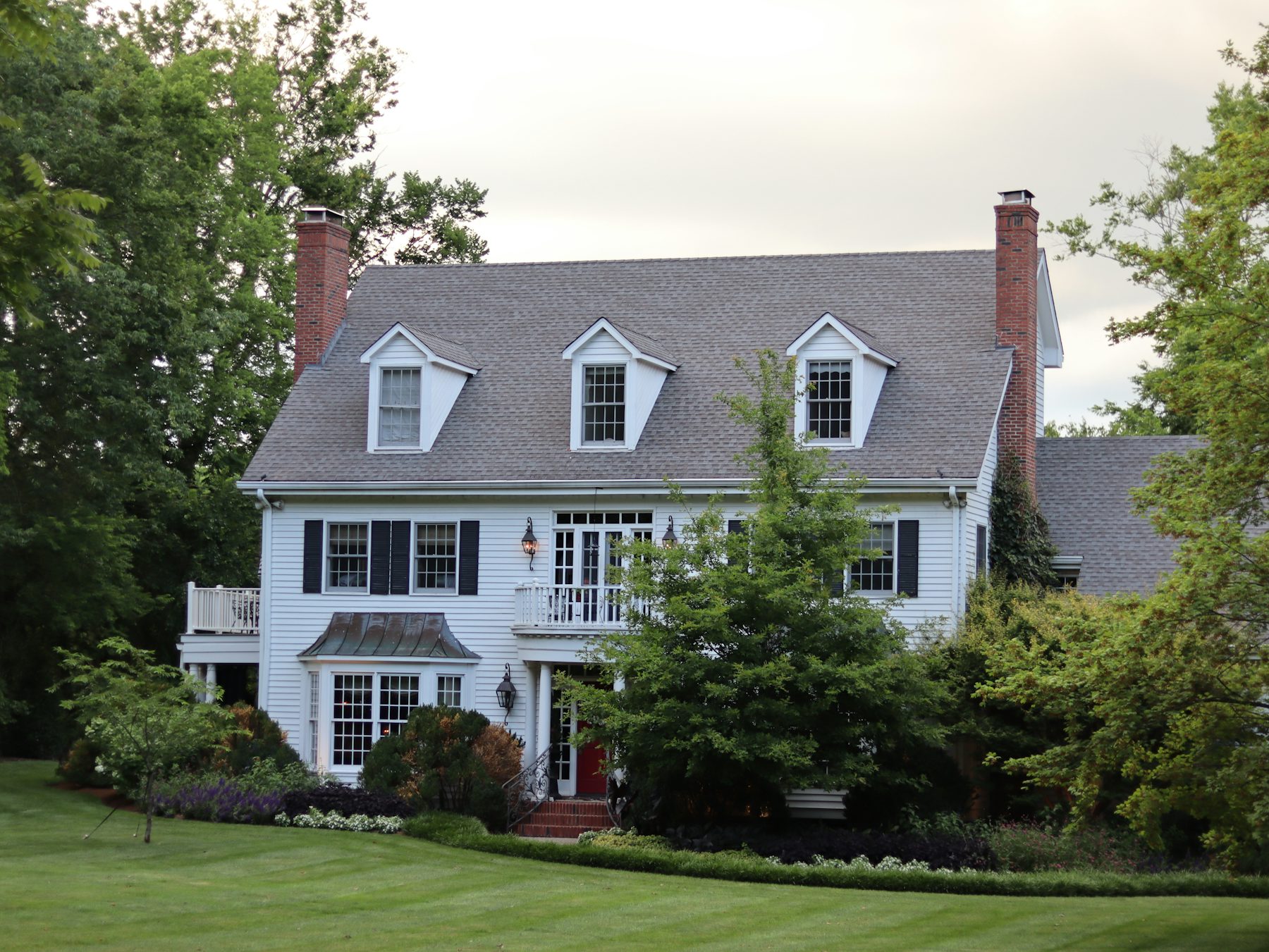 White colonial house with black shutters, dormers and brick chimneys above a green lawn