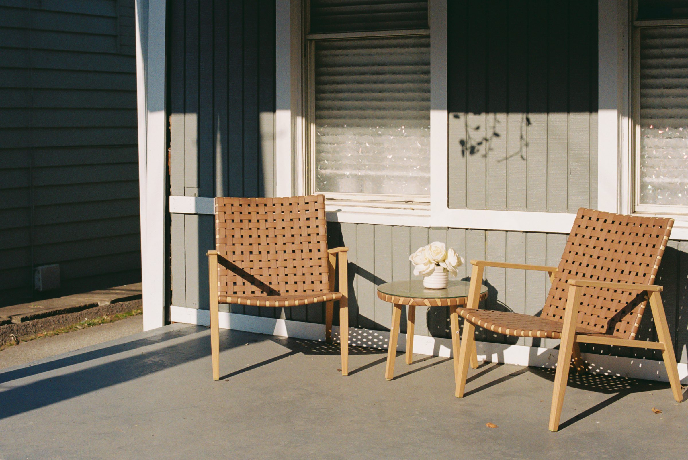 Pair of woven chairs and a small table on a sunlit porch