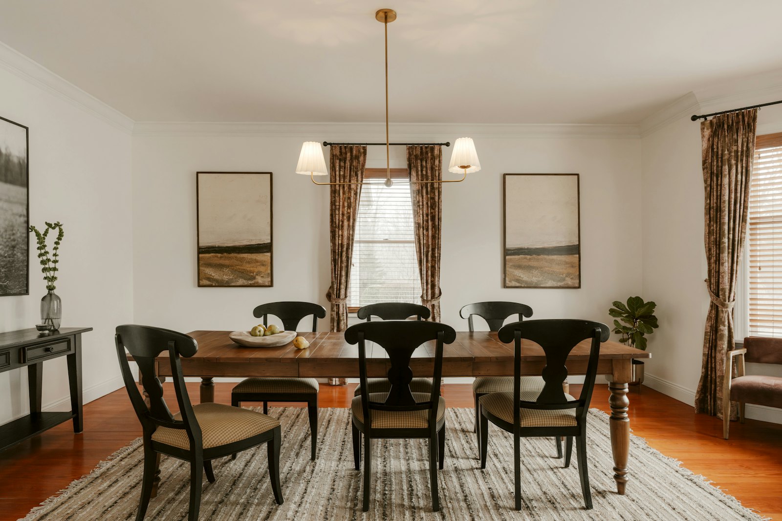 Dining room with a wooden table, black chairs and a brass pendant light
