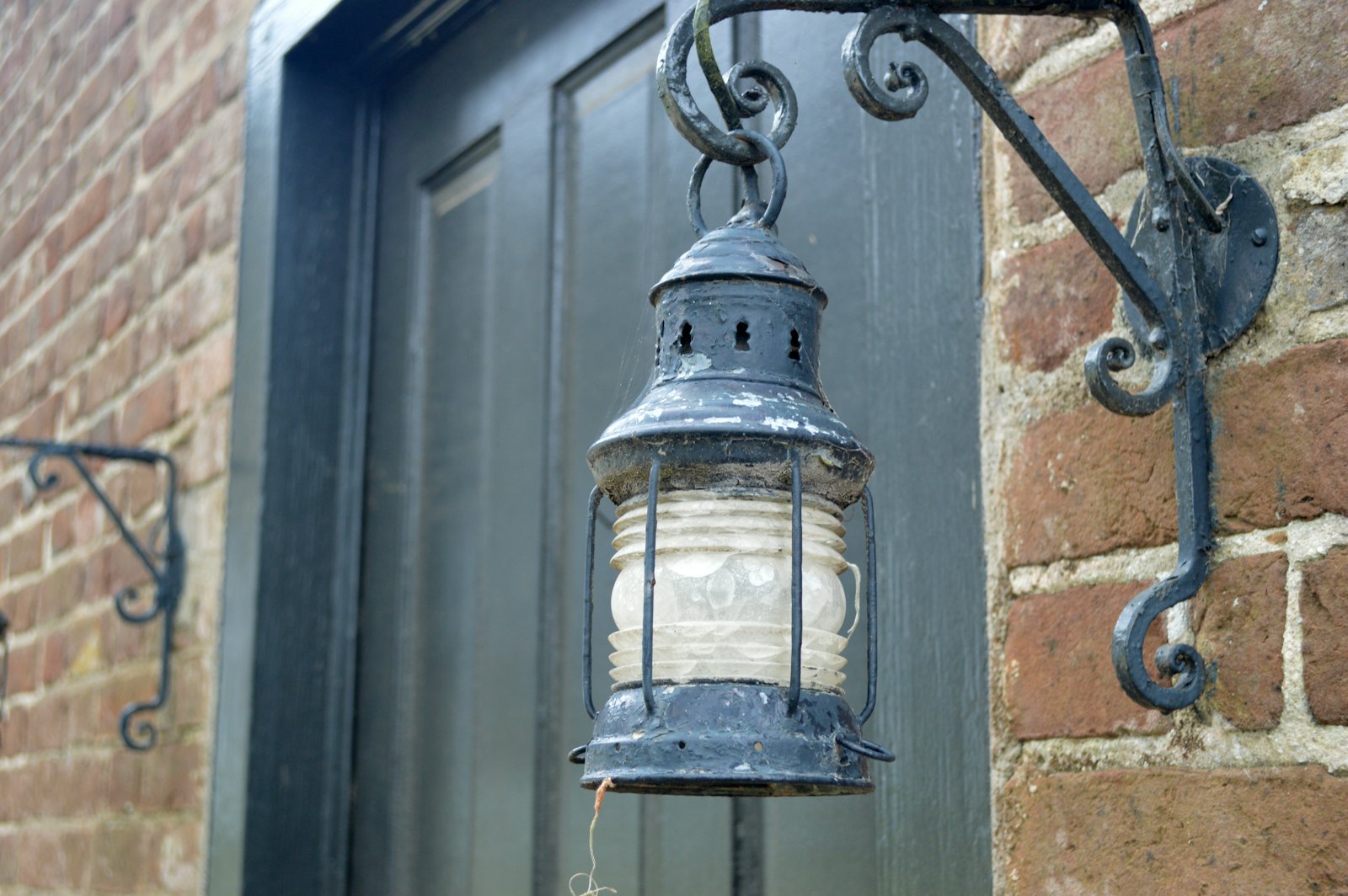 Weathered metal lantern mounted on a brick wall beside a door