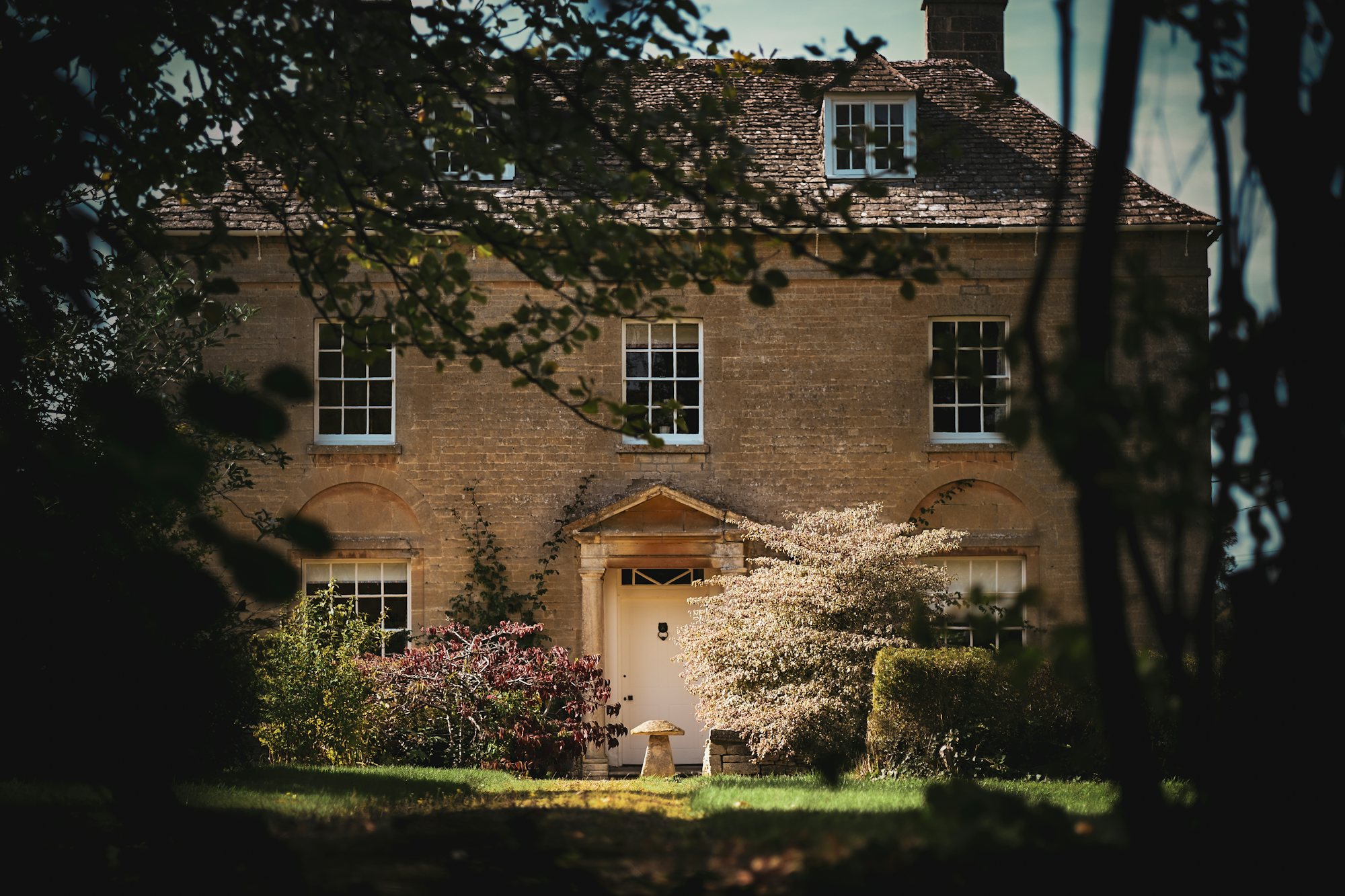 Stone manor house with a white door framed by trees